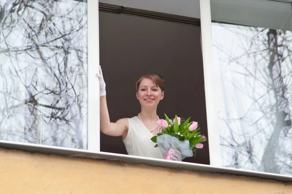 Young bride in home window opening with flowers — Stock Photo, Image