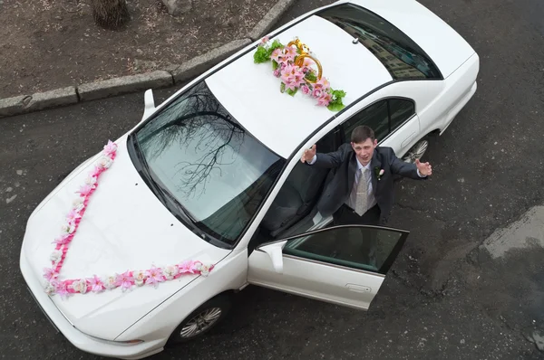 Novio recibir novia con abierto cerca de un auto blanco boda. — Foto de Stock