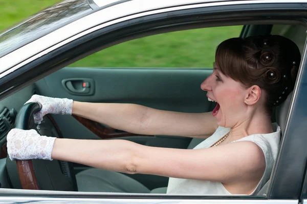 Žena v bílých šatech a bílých rukavicích sedí v autě jako řidič. — Stock fotografie