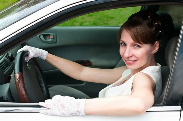 Mulher de vestido branco e luva branca sentada no carro como motorista . — Fotografia de Stock