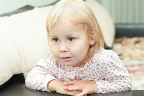 Petit enfant une fille blonde assise sur le canapé et regardant à travers — Photo