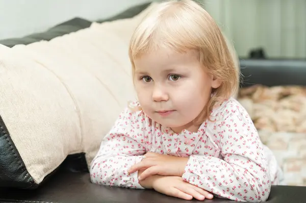 Criança uma menina loira sentada no sofá — Fotografia de Stock