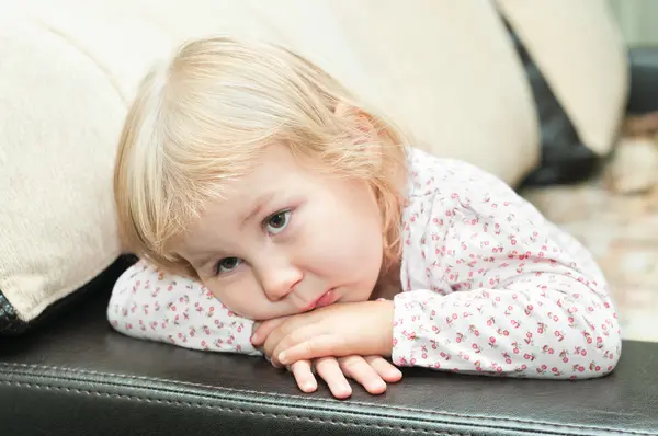 Kis gyerek egy dlond lány ül a kanapén, és vizsgálják át — Stock Fotó