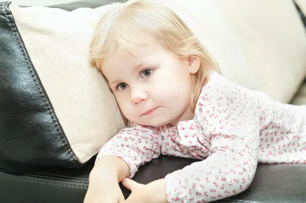 Little child a dlond girl sitting on sofa and looking through — Stock Photo, Image