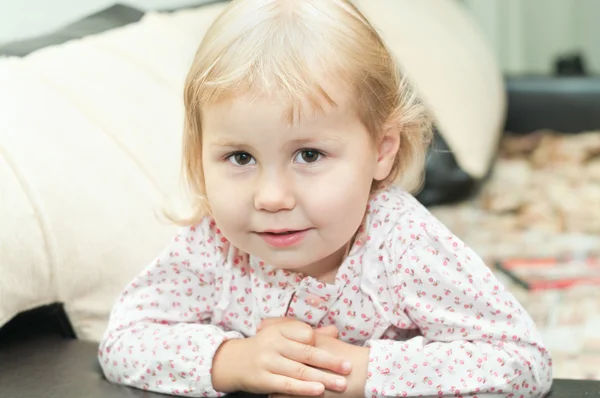 Little child a dlond girl sitting on sofa and looking through — Stock Photo, Image
