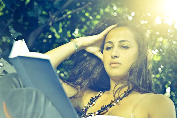 Mädchen im Park liest Buch mit Sonnenhintergrundbeleuchtung — Stockfoto
