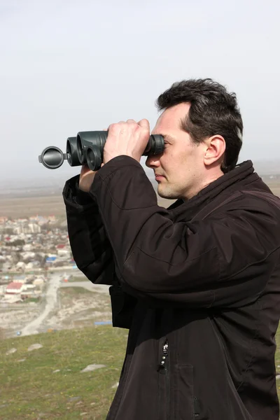 Man looks through binoculars — Stock Photo, Image