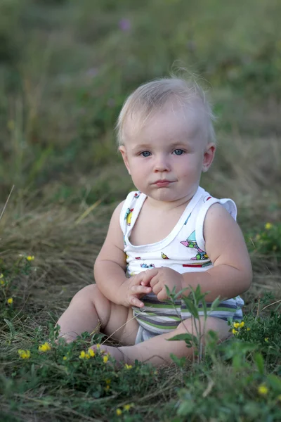 Bebê senta-se na grama — Fotografia de Stock