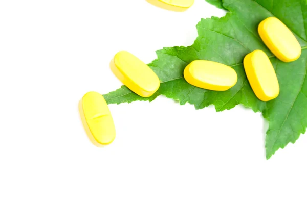 Píldoras de vitaminas amarillas sobre hoja verde — Foto de Stock