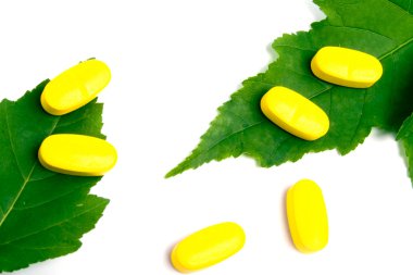 Sarı vitamin hapları üzerinde yeşil yaprakları