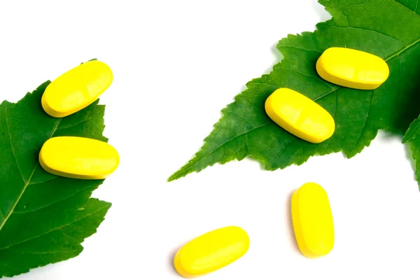 Pilules de vitamines jaunes sur les feuilles vertes — Photo
