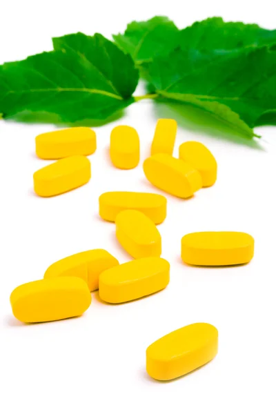 Sarı vitamin hapları üzerinde yeşil yaprakları — Stok fotoğraf
