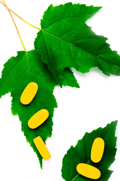 Píldoras amarillas de vitaminas sobre hojas verdes — Foto de Stock