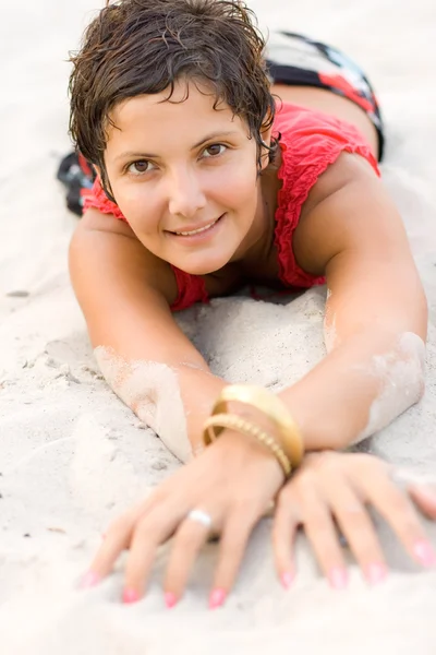 Brunet woman in red lying on a sand — Stock Photo, Image