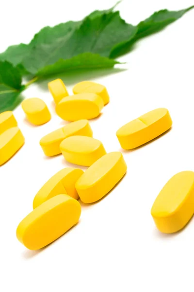 Yellow vitamin pills over green leaves — Stock Photo, Image