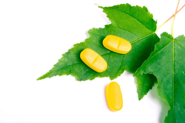 Píldoras amarillas de vitaminas sobre hojas verdes —  Fotos de Stock