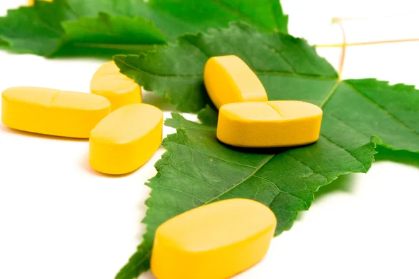 Vitamin pills over green leaves — Stock Photo, Image