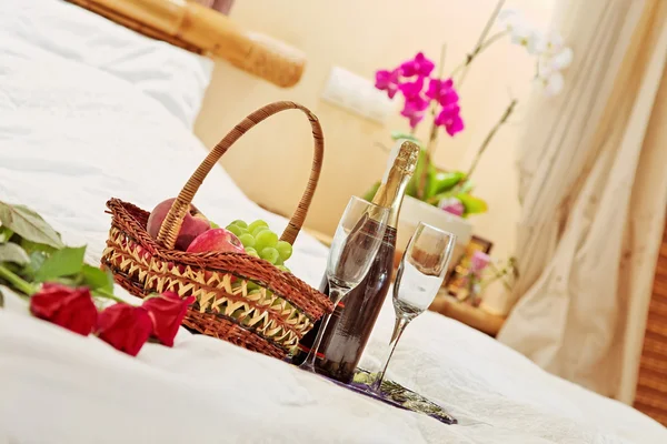 Троянди, фруктовий кошик і келихи для вина на чайній підносі в ліжку — стокове фото