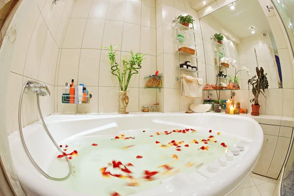 Banheiro moderno em tons quentes com jacuzzi e pétalas de rosa — Fotografia de Stock