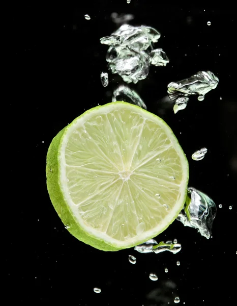 Lime (lemon) falling in water on black Royalty Free Stock Photos