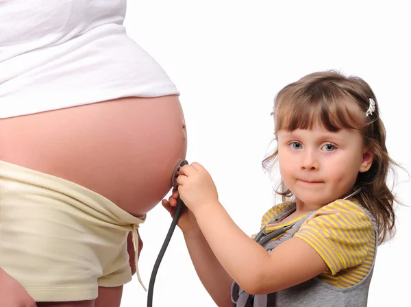 Pequeña niña escucha un estetoscopio vientre —  Fotos de Stock