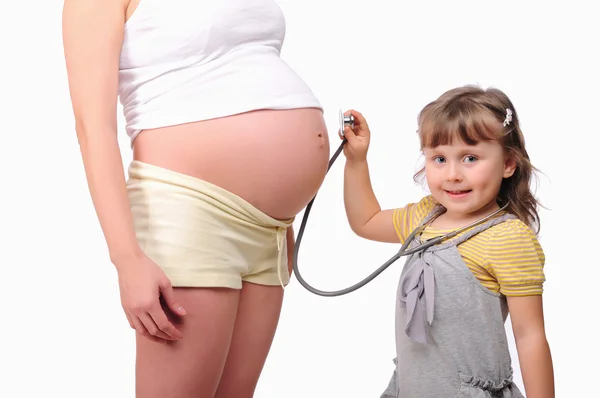 Pequeña niña escucha un estetoscopio vientre — Foto de Stock