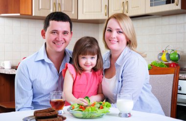 Dad, Mom and their little daughter lunching together in his kitchen. clipart