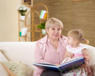 Grandmother reading a book to her granddaghter at home clipart