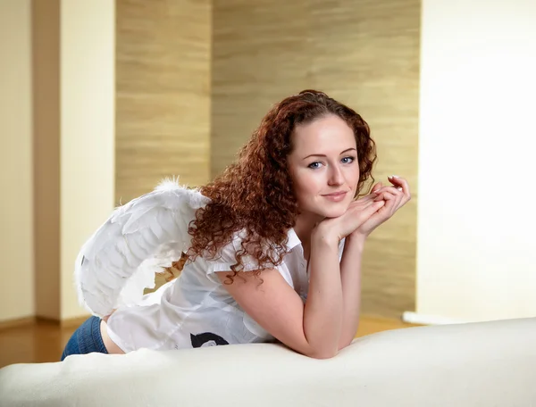 天使的翅膀坐在沙发上的年轻的红头发女人 — 图库照片