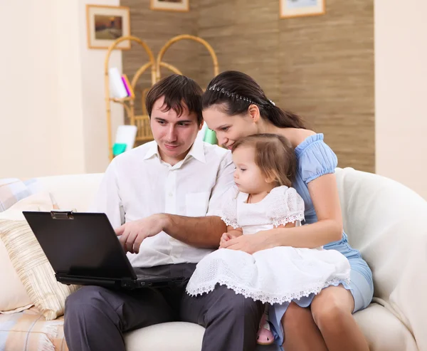 Jeune famille à la maison avec un ordinateur portable — Photo