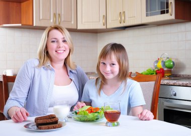 Mom and young daughter eating breakfast together in the kitchen clipart