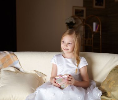 güzel, küçük bir kız evde hediye ile bir kanepede oturan beyaz elbiseli
