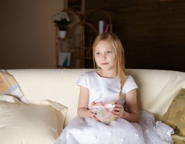 güzel, küçük bir kız evde hediye ile bir kanepede oturan beyaz elbiseli