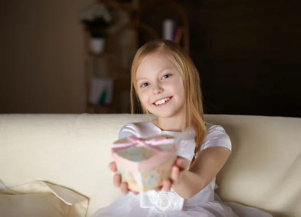 在白色的裙子 坐在一张沙发 一份礼物在家里上漂亮的小女孩 — 图库照片