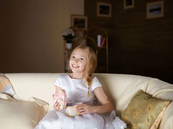 Ένα Όμορφο Κοριτσάκι Λευκό Φόρεμα Καθμένος Έναν Καναπέ Ένα Δώρο — Φωτογραφία Αρχείου