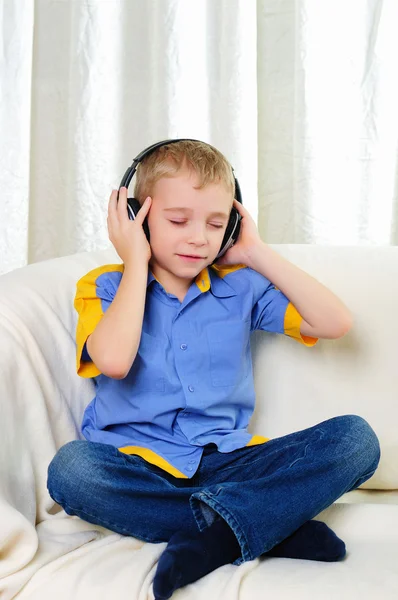 一个小男孩坐在一张沙发上耳机听音乐 — 图库照片