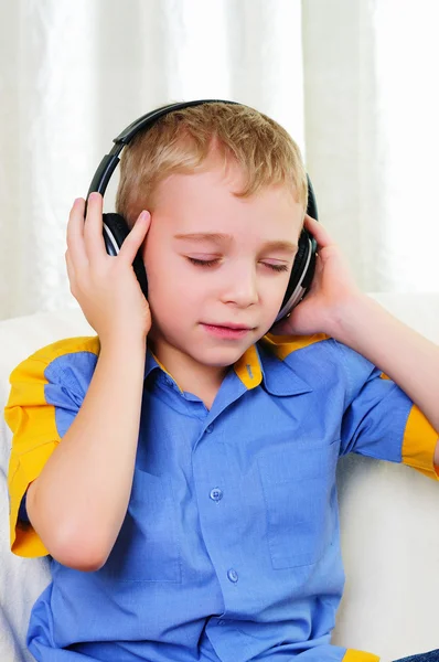Lille Dreng Sidder Sofa Med Hovedtelefoner Lytter Musik - Stock-foto