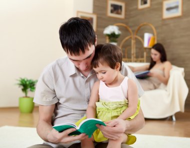 Young father with a daughter at home reading a book clipart