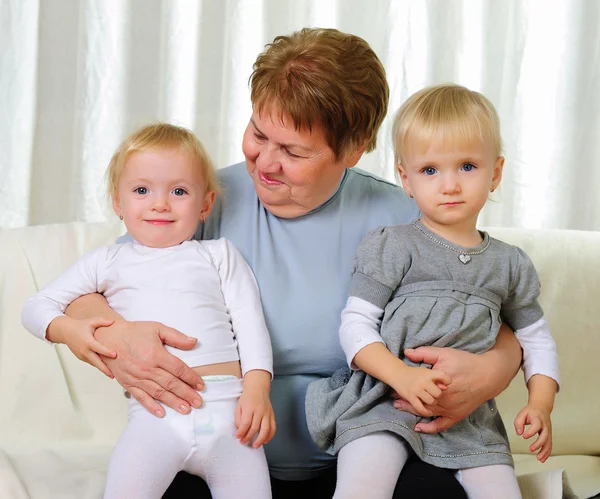 两个双胞胎姐妹与他们的祖母坐在沙发上 — 图库照片