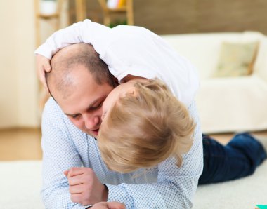 Little boy and his father playing together at home on the floor clipart