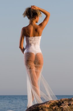 Young bride stands on a rock near the sea