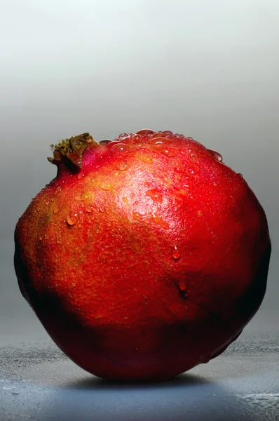 Pomegranate stands on the wet gray background — Stock Photo, Image