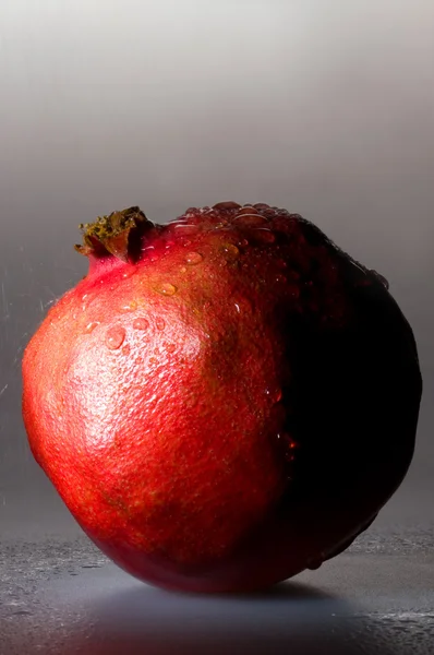 Pomegranate stands on the wet gray background — Stock Photo, Image