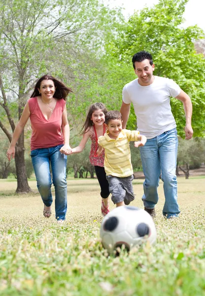 Pais e duas crianças pequenas jogando futebol no campo verde — Fotografia de Stock