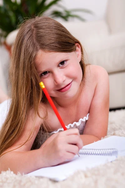 Glimlachend jong meisje liegen en schrijven in notitieblok — Stockfoto