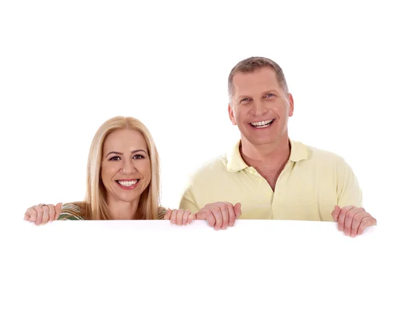 Paar mittleren Alters steht hinter einer weißen Tafel und lächelt — Stockfoto