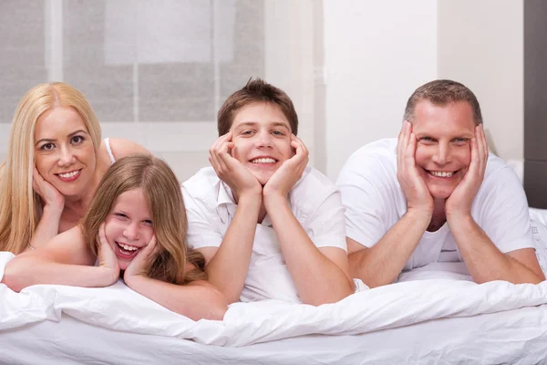 Schöne Familie, die lächelnd auf dem Bett liegt und dich ansieht — Stockfoto