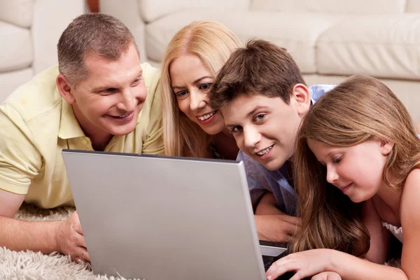 Familia acostada en la alfombra en la sala de estar con ordenador portátil —  Fotos de Stock