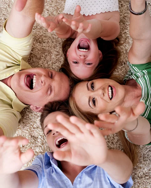 Família feliz de quatro deitado no tapete — Fotografia de Stock