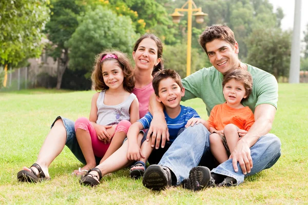 Семья сидит в парке и улыбается в камеру Стоковое Изображение